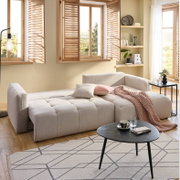 Gemütliche Rundecke in einem modernen Wohnzimmer, aus der Perspektive von vorne links fotografiert. Die Couch ist in ein helles Beige gehüllt und mit Kissen und einer Decke dekoriert.