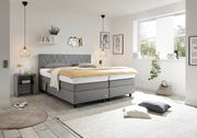Modernes Boxspringbett in einem hellen Schlafzimmer, seitliche Perspektive, mit grauem Kopfteil und eleganter Dekoration.