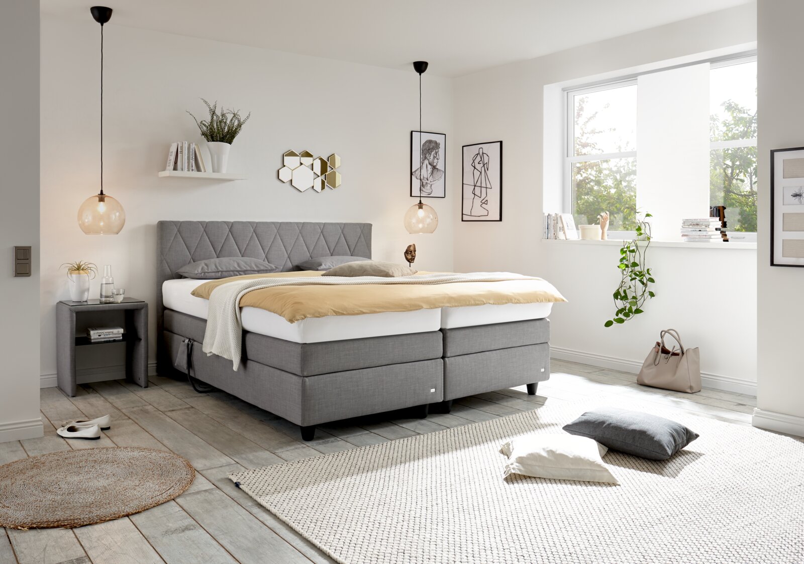 Modernes Boxspringbett in einem hellen Schlafzimmer, seitliche Perspektive, mit grauem Kopfteil und eleganter Dekoration.