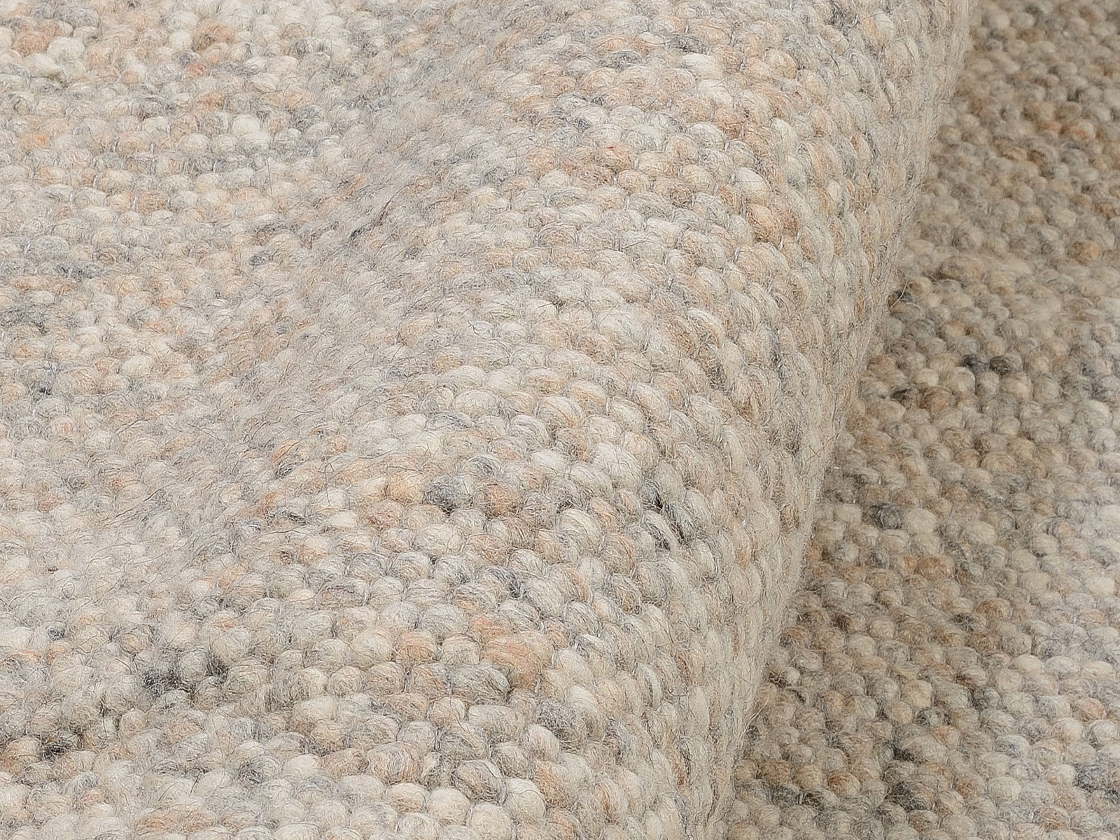 Nahaufnahme eines handgewebten Teppichs in natürlichen Beige- und Grautönen, seitliche Perspektive