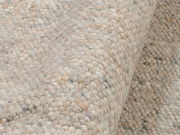 Nahaufnahme eines handgewebten Teppichs in natürlichen Beige- und Grautönen, seitliche Perspektive