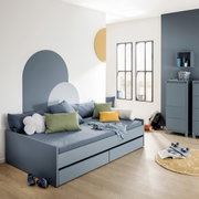 Modernes Bodenbett in einem stilvollen Raum mit blauen und grünen Kissen, zwei Schubladen und einem dekorativen Wanddesign. Perspektive von vorne links.