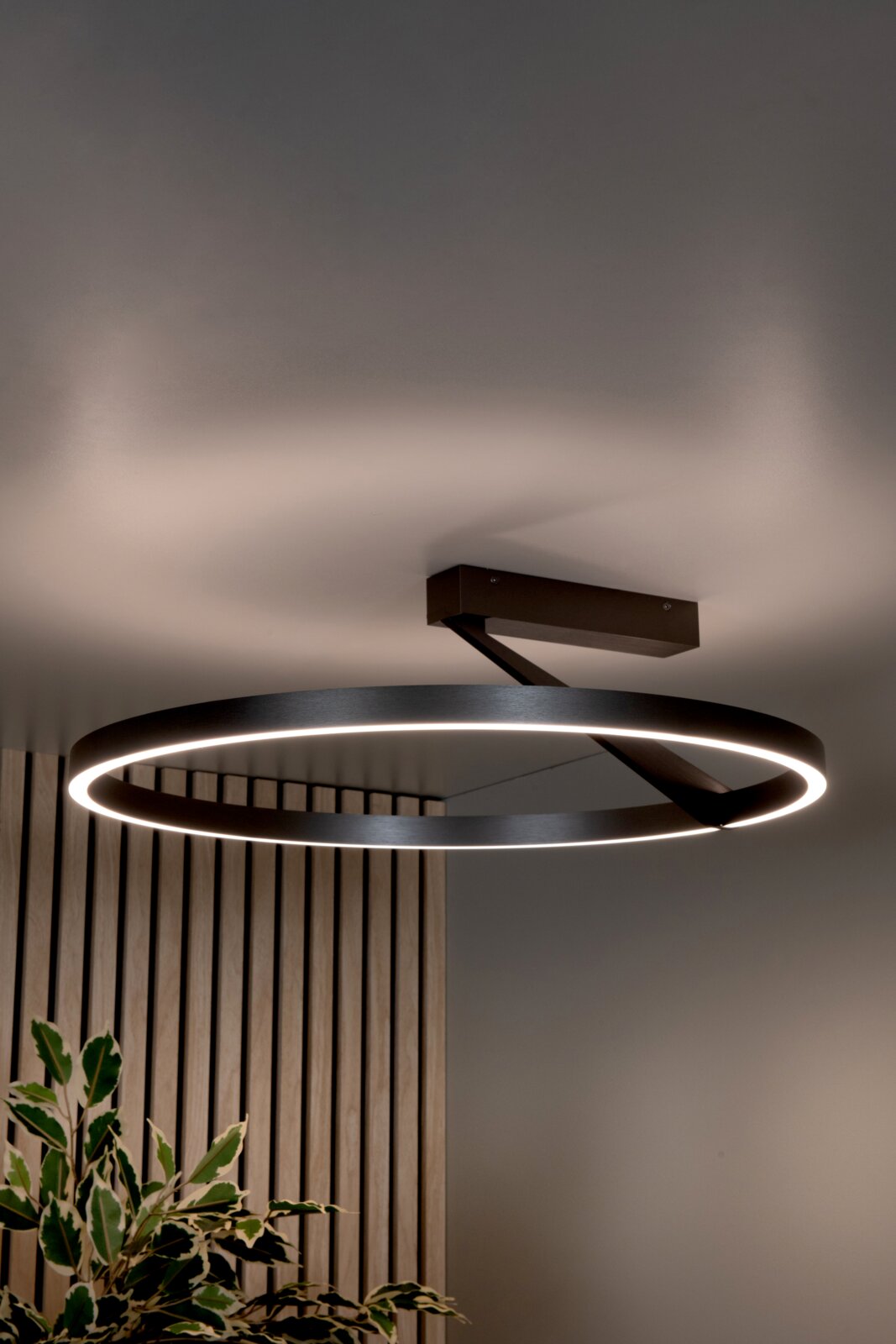 Moderne runde LED-Deckenleuchte in Ringform aus schwarzem Metall mit warmweißem Licht, an der Decke montiert – Ansicht leicht von unten im Innenraum
