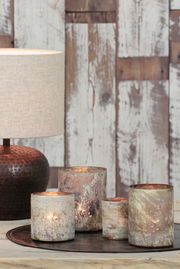 Lampenschirm in natürlichem Beige, seitliche Perspektive, auf einem Tisch mit dekorativen Kerzenhaltern vor einer rustikalen Holzwand.