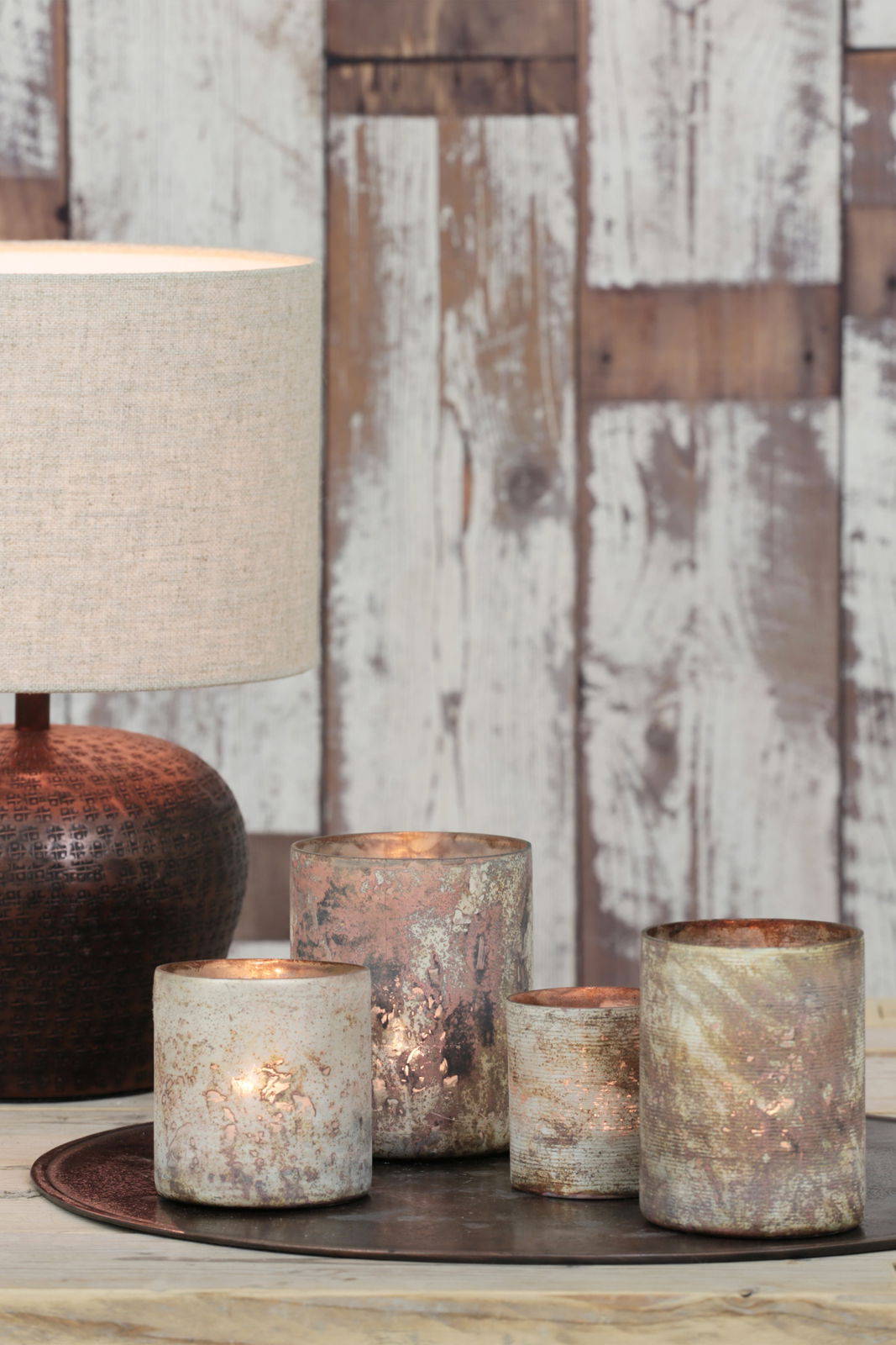 Lampenschirm in natürlichem Beige, seitliche Perspektive, auf einem Tisch mit dekorativen Kerzenhaltern vor einer rustikalen Holzwand.