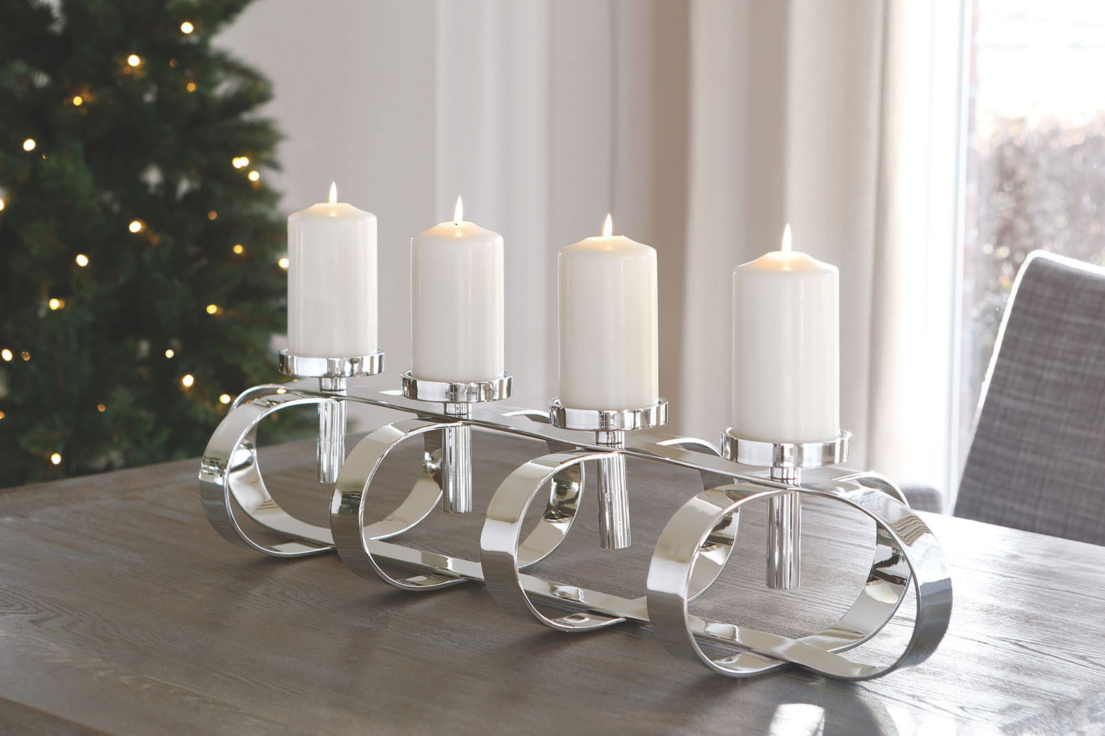 Moderner, vierflammiger Kerzenleuchter aus glänzendem Metall auf einem Tisch, seitliche Perspektive.