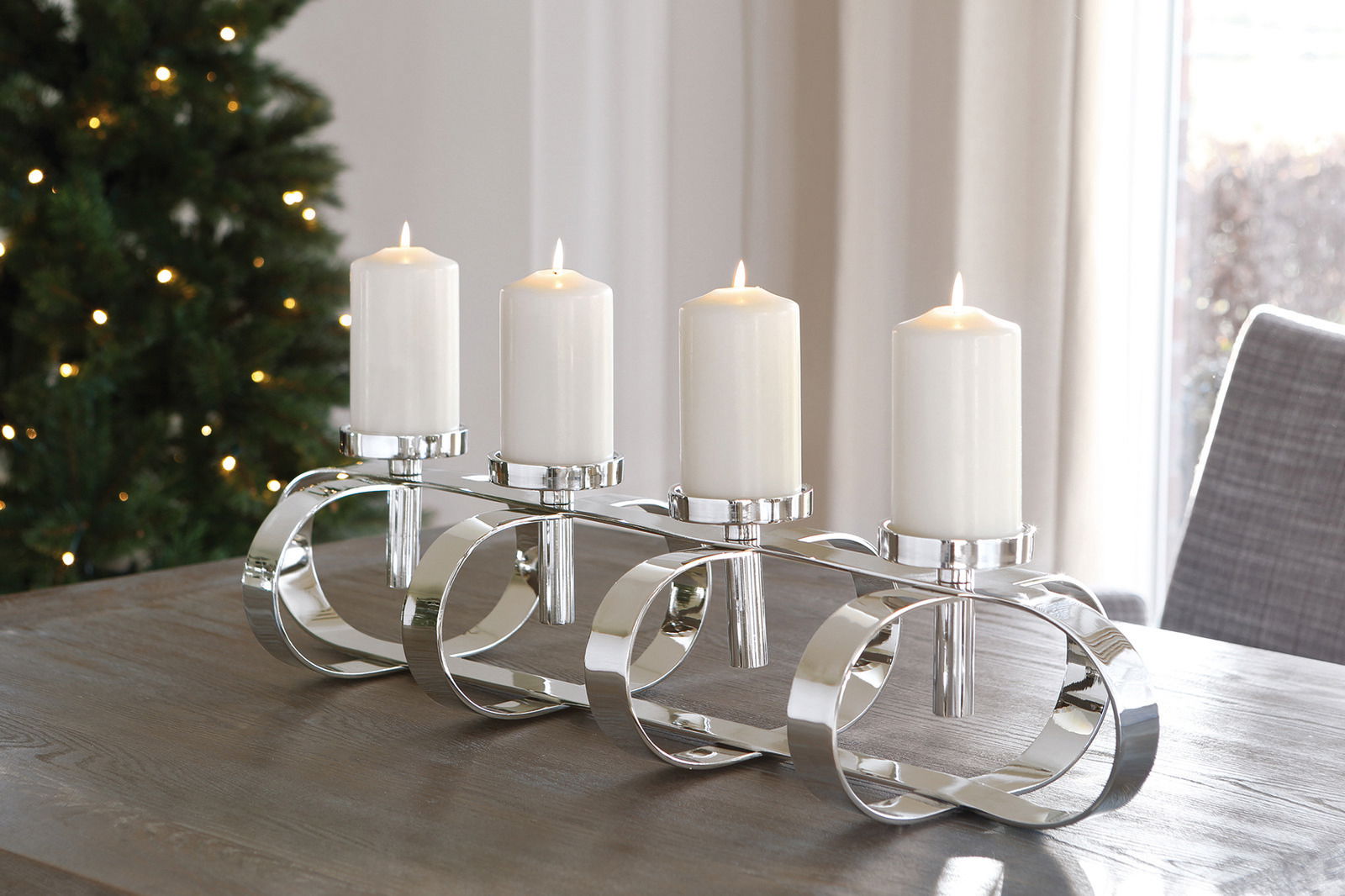 Moderner, vierflammiger Kerzenleuchter aus glänzendem Metall auf einem Tisch, seitliche Perspektive.