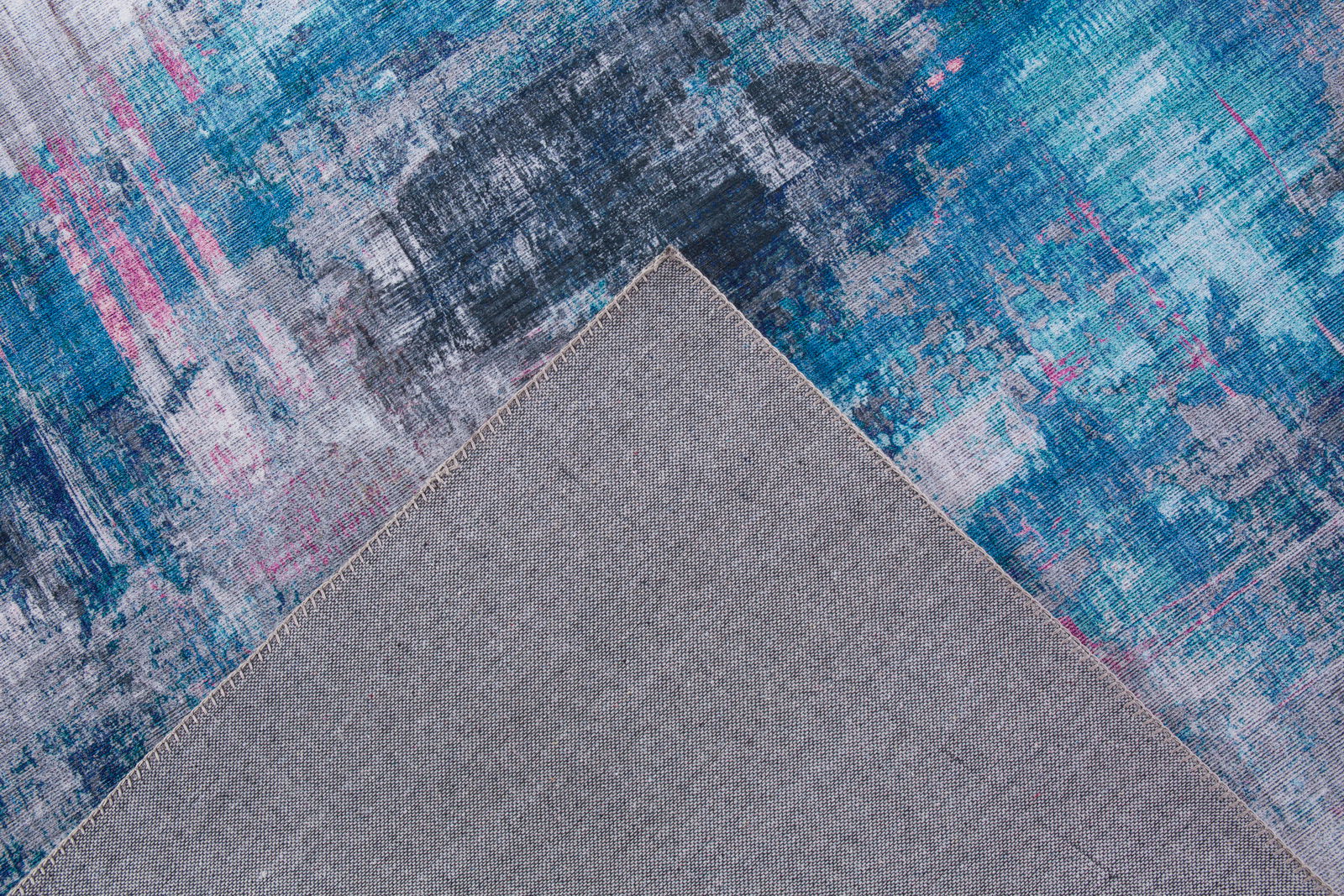 Teppich in Blau- und Grautönen mit abstraktem Muster, Perspektive von oben mit umgeschlagener Ecke