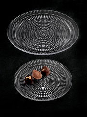 Zwei elegante, durchsichtige Glasteller mit strukturiertem Muster, von oben fotografiert. Auf dem kleineren Teller liegen drei Pralinen.