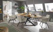 Moderner Esstisch mit ovaler Holzplatte und schwarzen Metallbeinen, umgeben von sechs beigen Stühlen in einem hellen Esszimmer mit Dachfenstern, seitliche Perspektive.