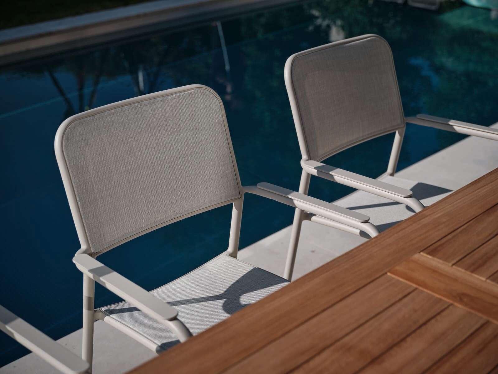 Zwei graue Stapelsessel aus Metall neben einem Pool, seitliche Perspektive