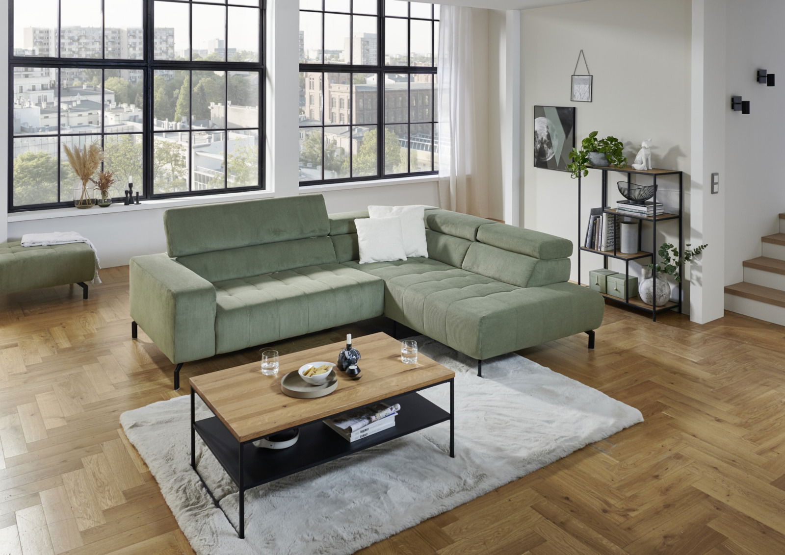 Grüne Eckgarnitur in modernem Wohnzimmer mit großen Fenstern, aus der Perspektive von vorne rechts.