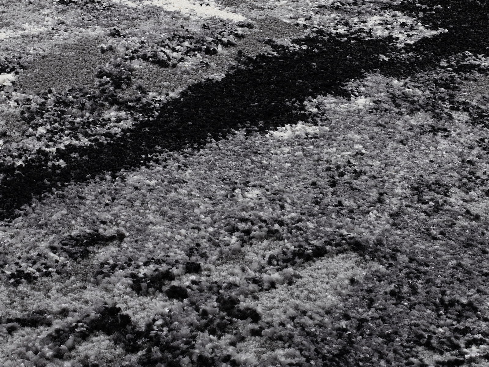 Nahaufnahme eines Designer-Teppichs mit abstraktem, schwarz-weißem Muster und flauschiger Textur, von oben betrachtet.