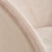 Close-up van een fauteuil met een zachte, beige stoffen bekleding en zichtbare stiksels, gezien vanaf de zijkant.