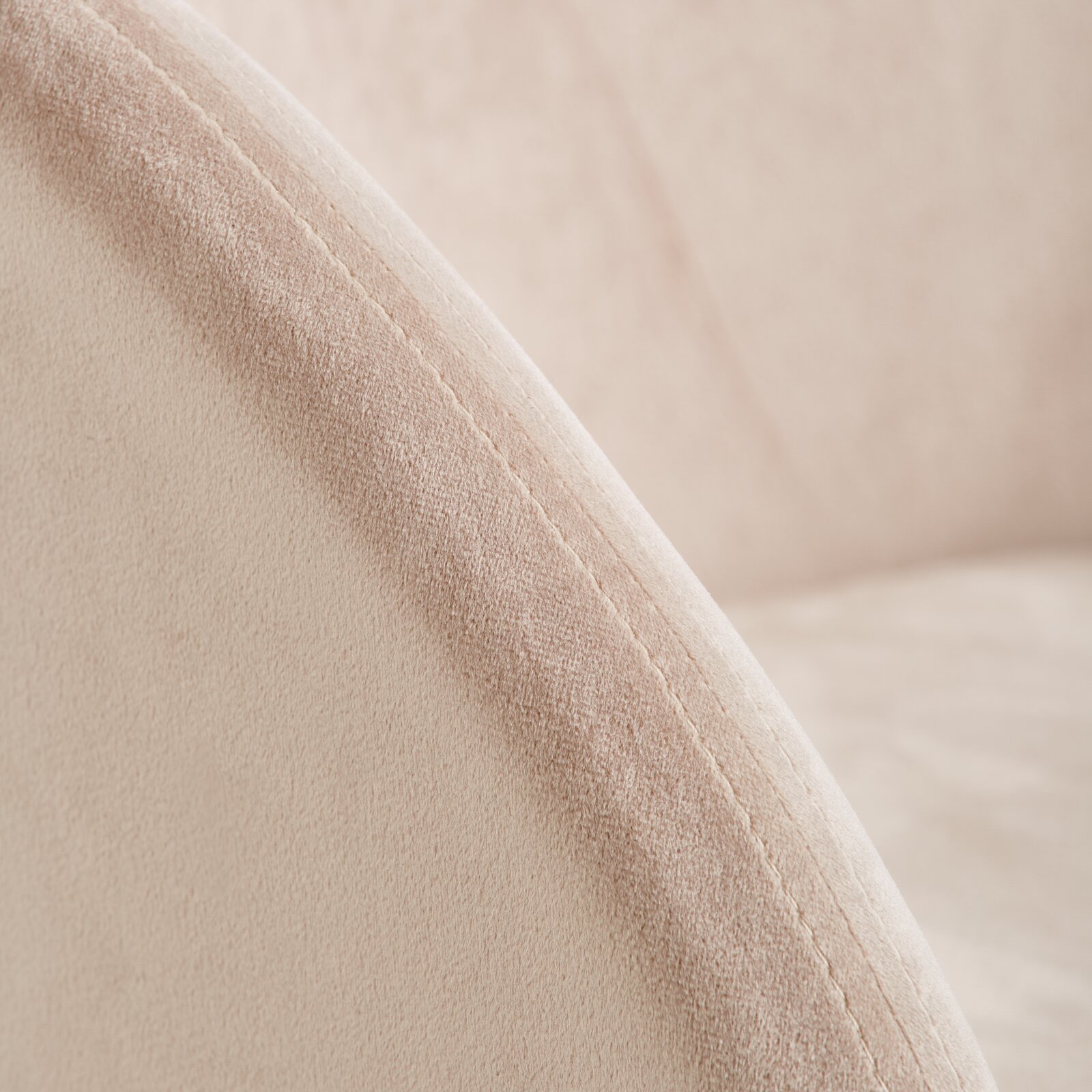 Close-up van een fauteuil met een zachte, beige stoffen bekleding en zichtbare stiksels, gezien vanaf de zijkant.