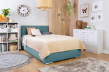 Gemütliches Schlafzimmer mit einem Boxbett in Türkis, dekoriert mit Kissen und einer beigen Steppdecke, umgeben von modernen Möbeln und Pflanzen. Perspektive von schräg vorne.