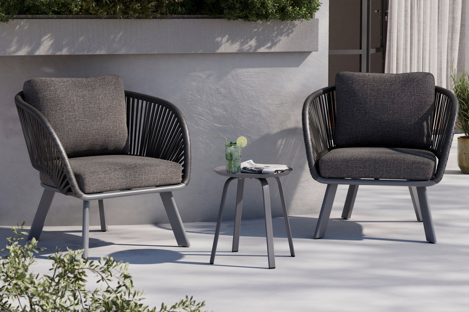 Moderner Beistelltisch aus Metall in einer Außenumgebung, umgeben von zwei grauen Sesseln, mit einem Getränk und einer Zeitung darauf, seitliche Perspektive.