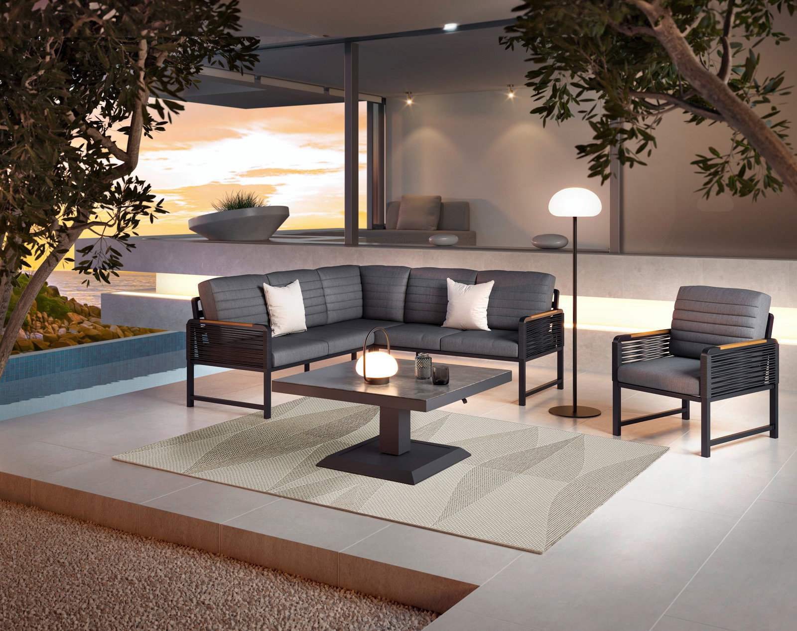 Moderne Loungegarnitur mit grauen Polstern und schwarzem Gestell, bestehend aus Sofa, Sessel und Tisch, auf einer Terrasse mit Blick auf den Sonnenuntergang.
