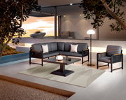Een moderne loungeset met grijze bekleding en een zwart frame, bestaande uit een bank, een fauteuil en een tafel, op een terras met uitzicht op de zonsondergang.