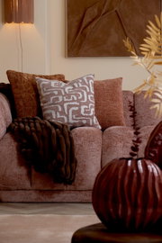 Vooraanzicht van een warme terracottakleurige bank met decoratieve sierkussens en een donkerbruine plaid in een sfeervol interieur.