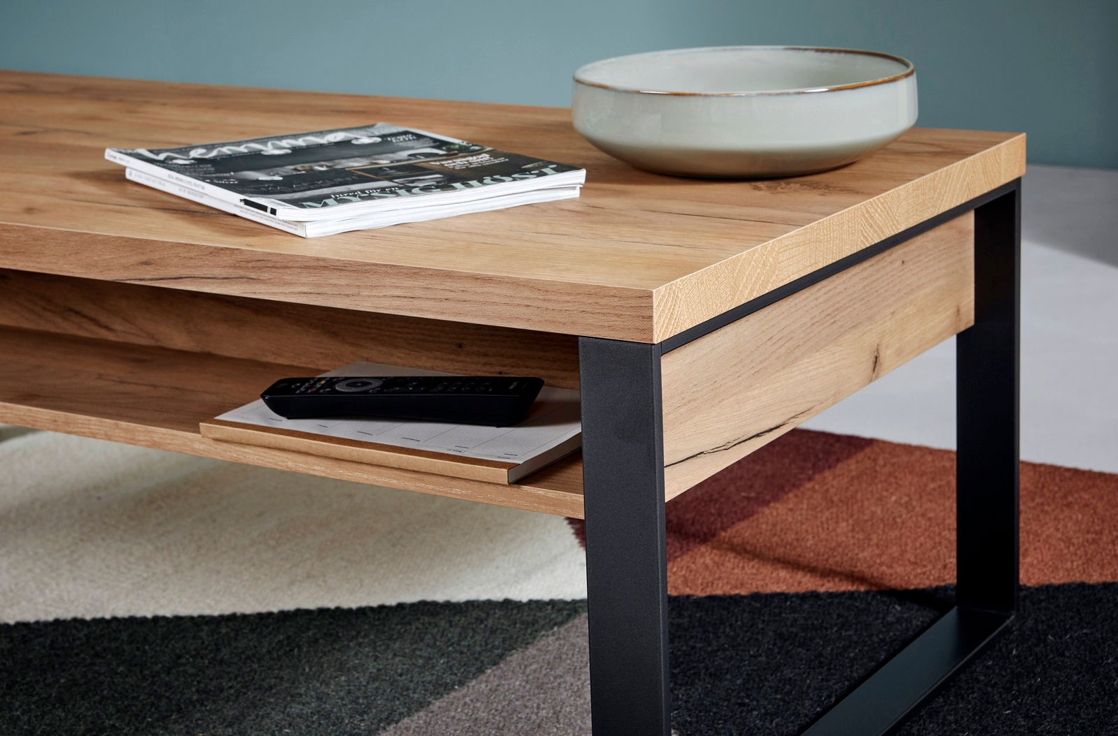 Moderner Couchtisch aus Holz mit schwarzem Metallgestell, seitliche Perspektive, mit Zeitschriften und Schale dekoriert.