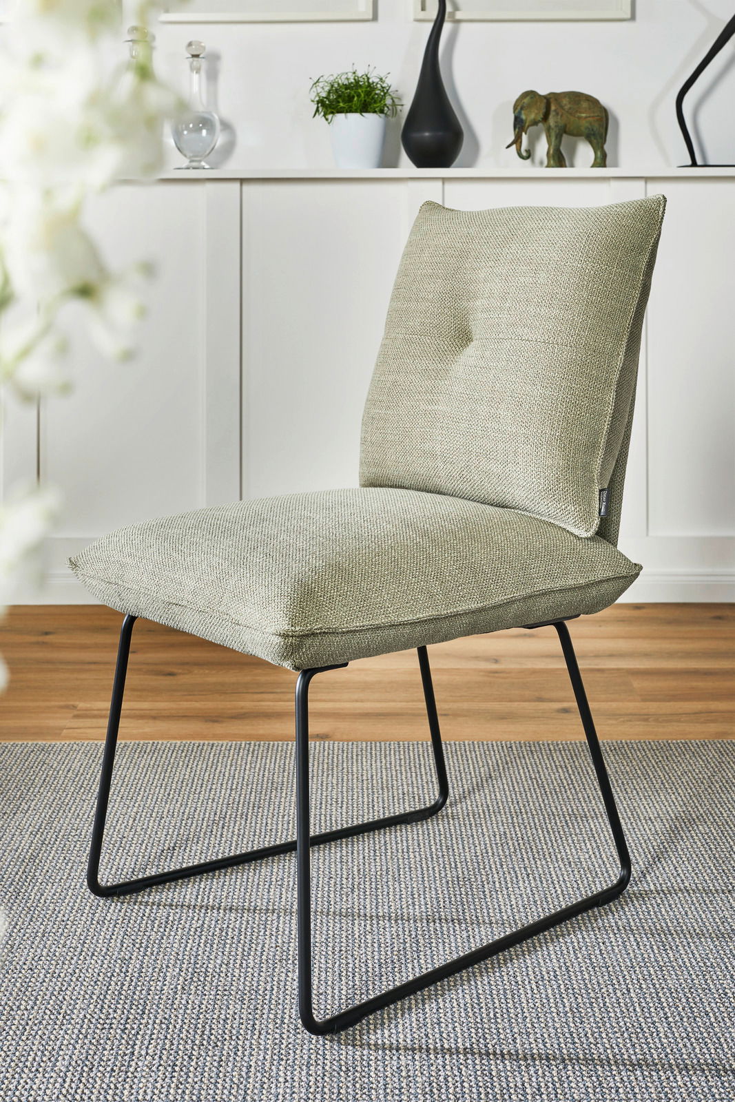 Moderner Stuhl mit grünem Stoffbezug und schwarzem Metallgestell, seitliche Perspektive