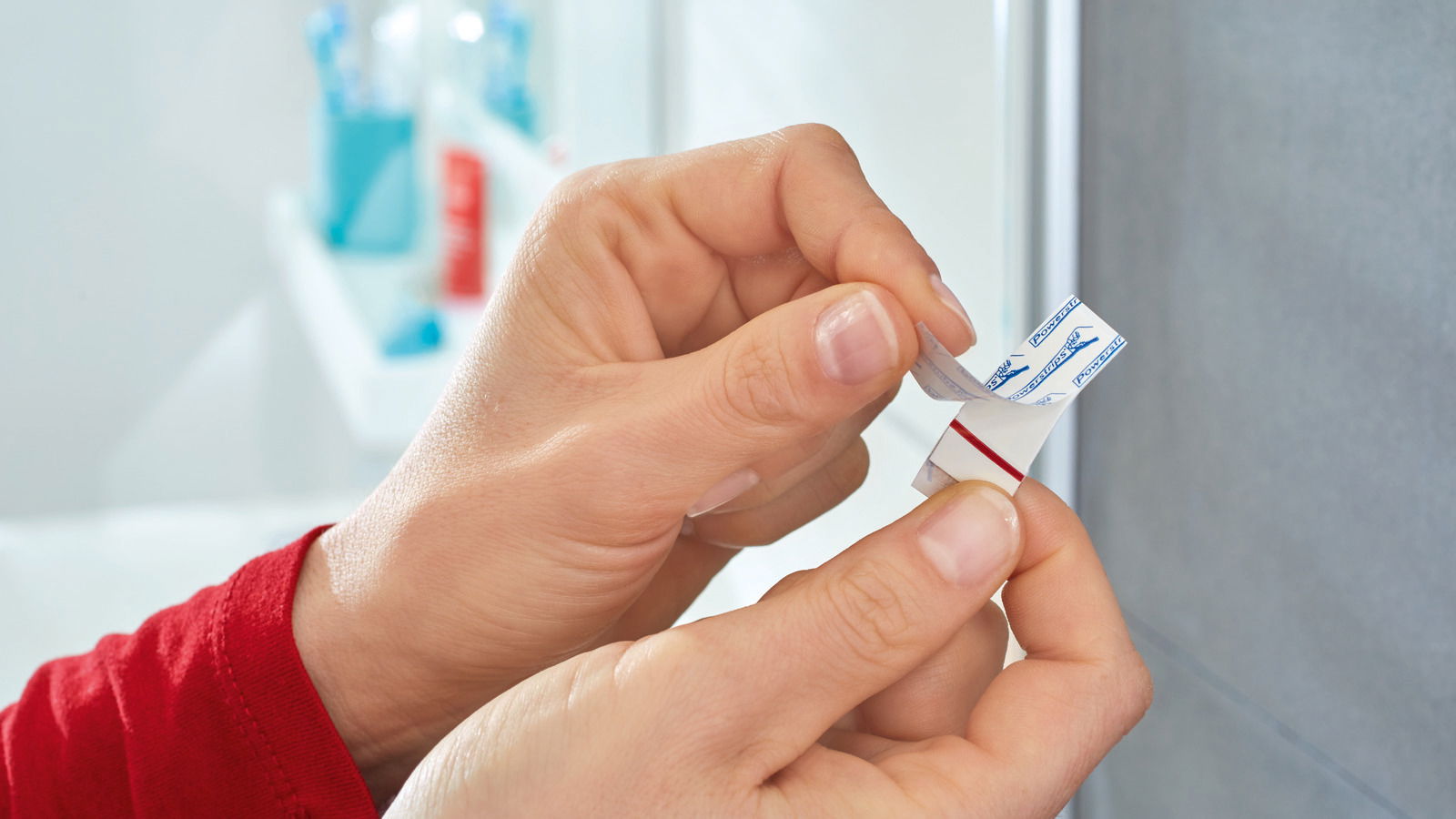 Nahaufnahme von Händen, die einen tesa Powerstrip Waterproof an einer Wand anbringen.