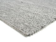 Nahaufnahme eines handgewebten Teppichs in Grautönen, schräg von der Seite fotografiert.