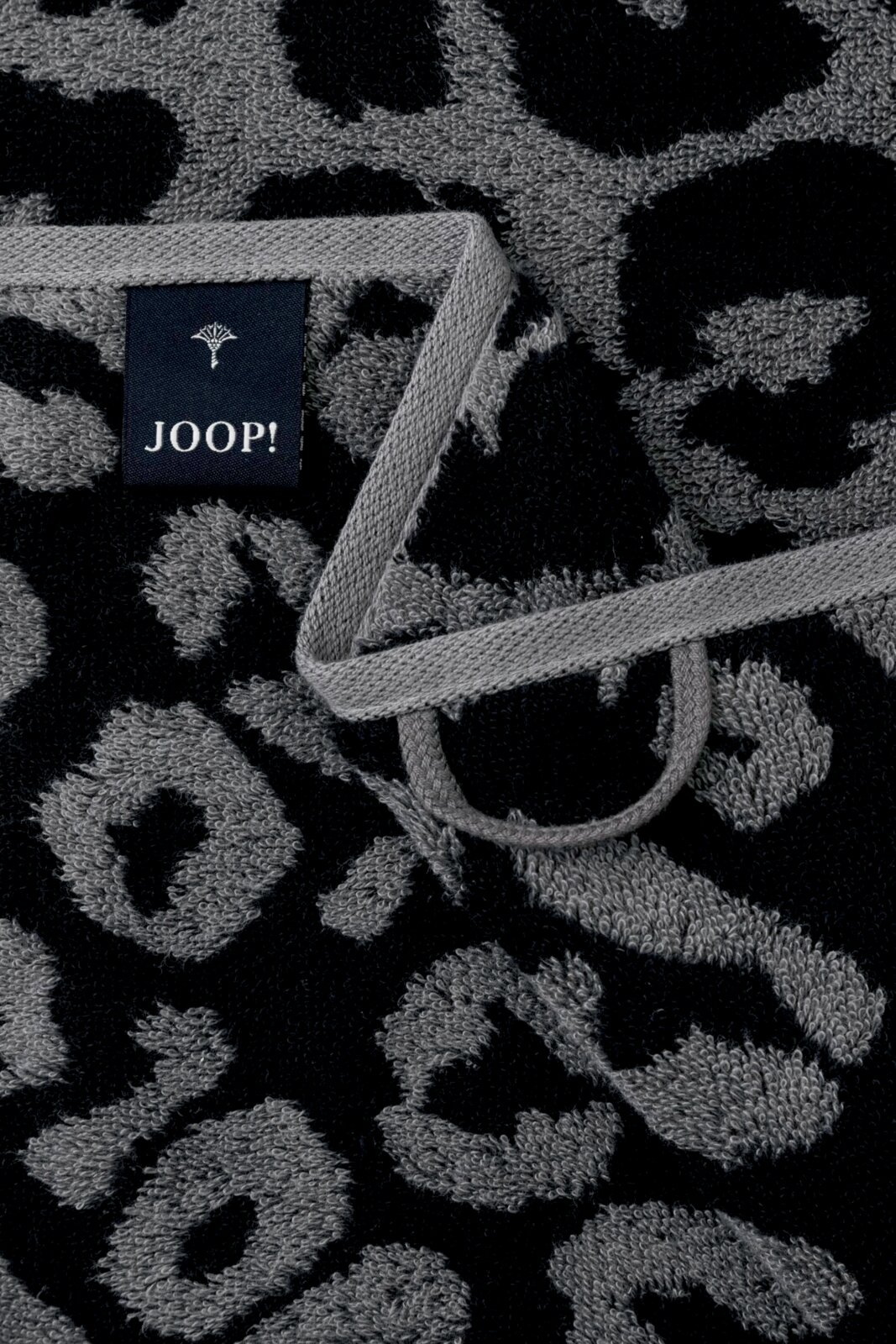 Nahaufnahme eines grauen Gästetuchs mit schwarzem Leopardenmuster und einem Joop-Label.