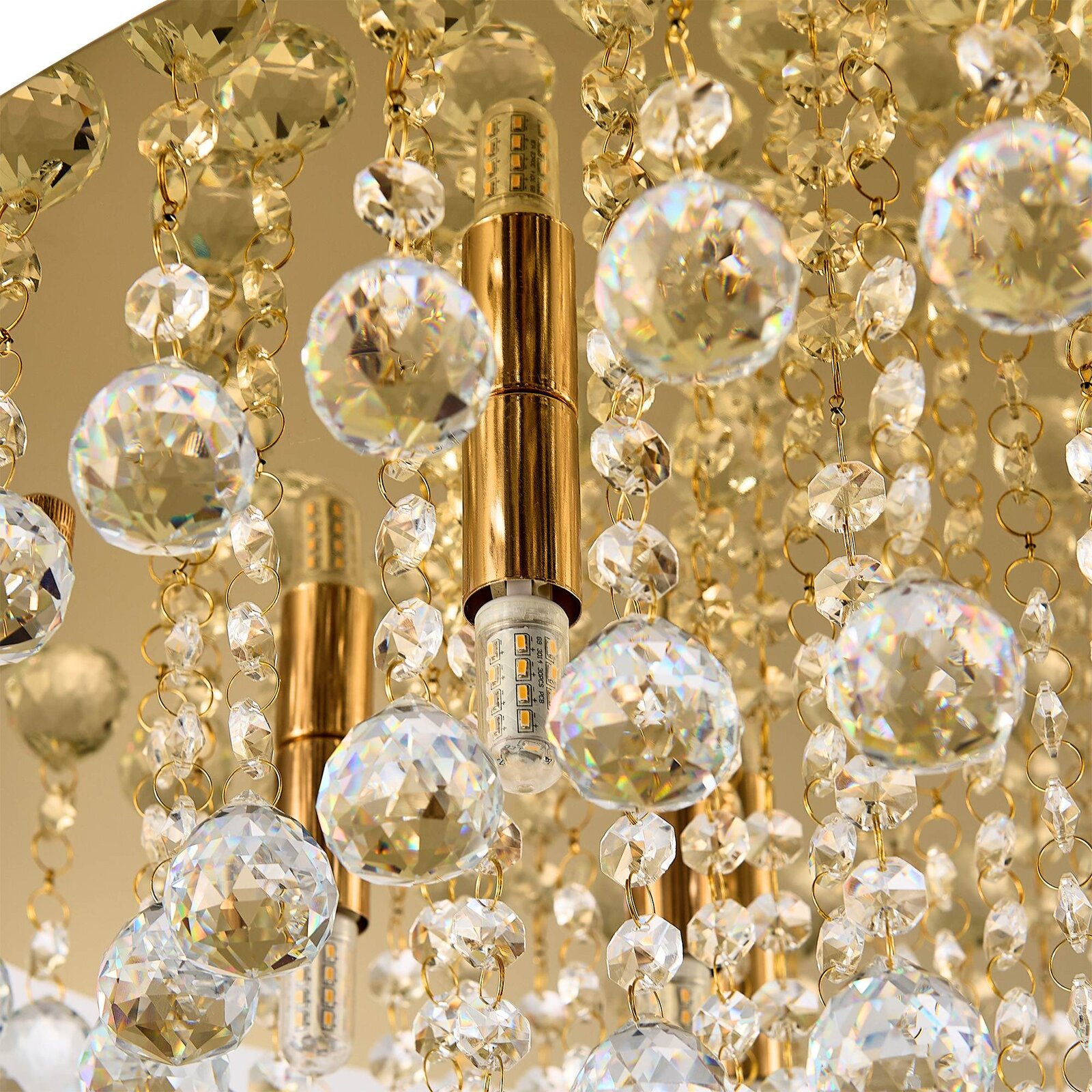 Nahaufnahme einer luxuriösen Deckenleuchte mit goldenen Elementen und funkelnden Kristallanhängern, von unten betrachtet.