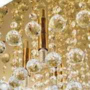 Nahaufnahme einer luxuriösen Deckenleuchte mit goldenen Elementen und funkelnden Kristallanhängern, von unten betrachtet.