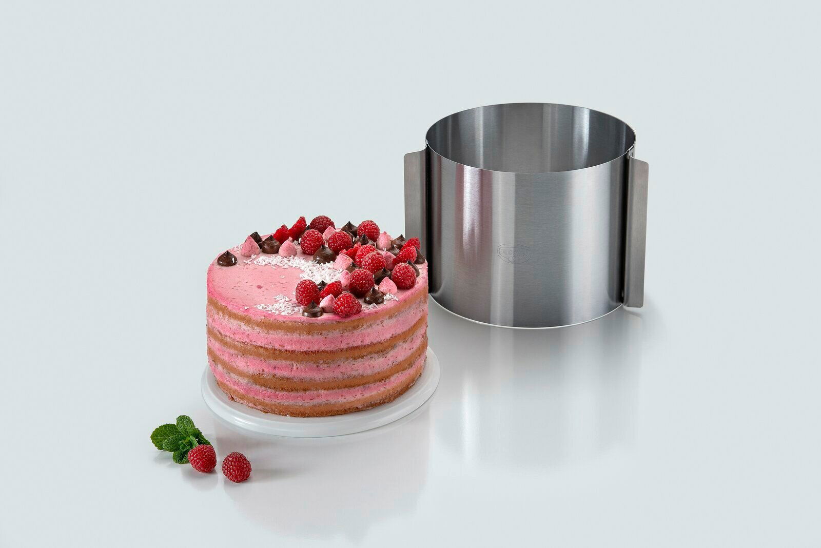 Tortenring extra hoch 15 cm aus Edelstahl neben einer dekorierten Torte mit Himbeeren, seitliche Perspektive.