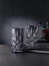 Zwei elegante Longdrinkgläser aus Kristallglas mit facettiertem Design, frontal auf einem dunklen Hintergrund präsentiert.