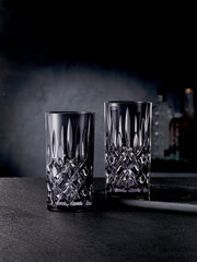 Zwei elegante Longdrinkgläser aus Kristallglas mit facettiertem Design, frontal auf einem dunklen Hintergrund präsentiert.