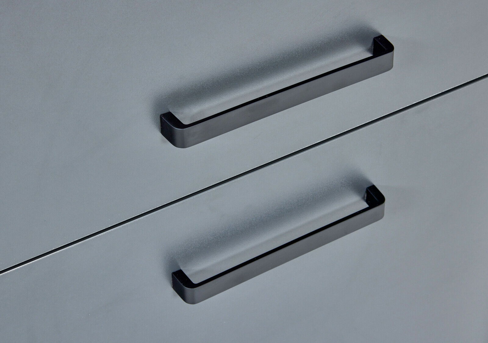 Nahaufnahme von zwei schwarzen Griffen an einer grauen Schranktür, seitliche Perspektive