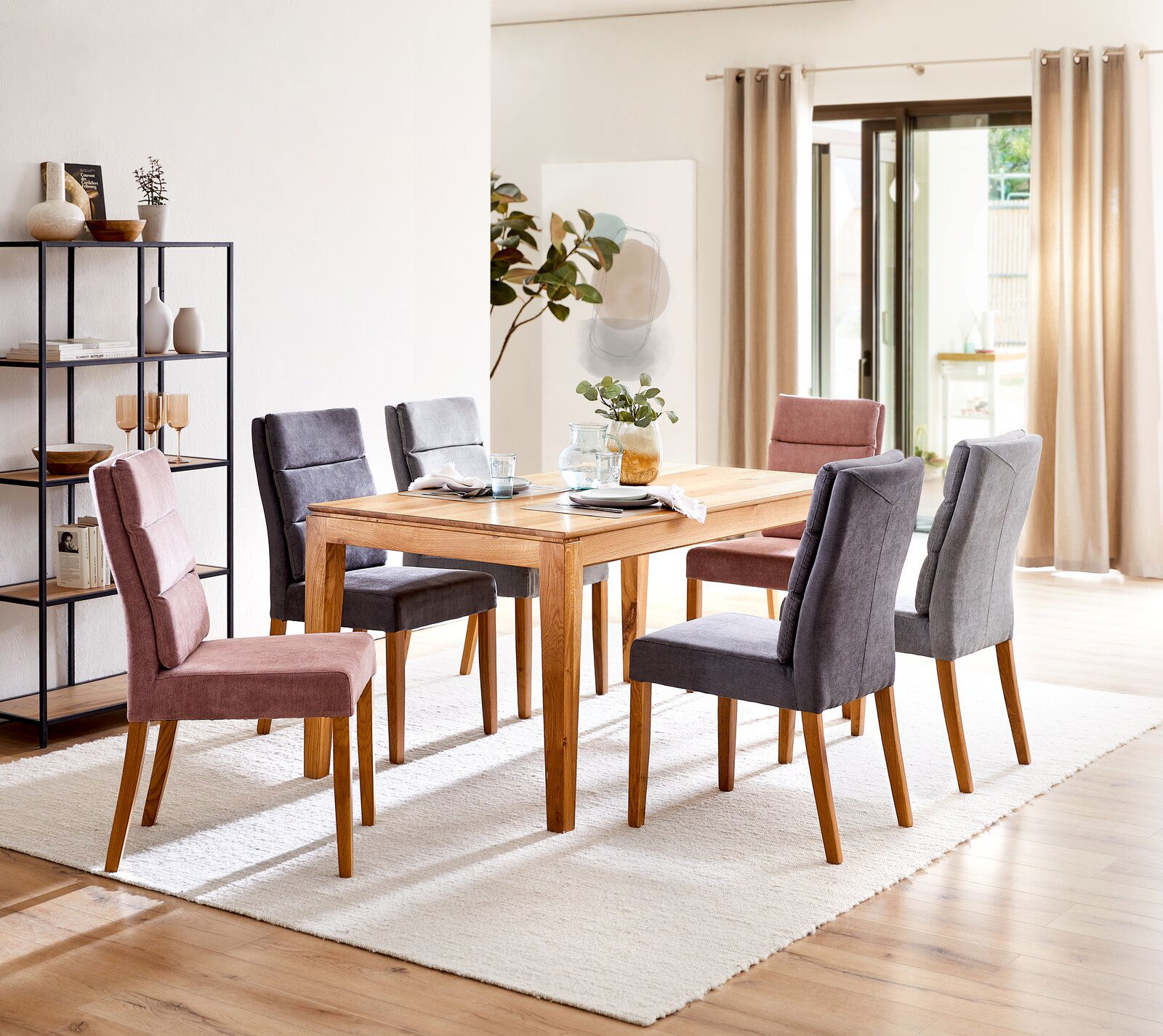 Esszimmer mit einem Holztisch und sechs gepolsterten Stühlen in Grau und Rosa, seitliche Perspektive