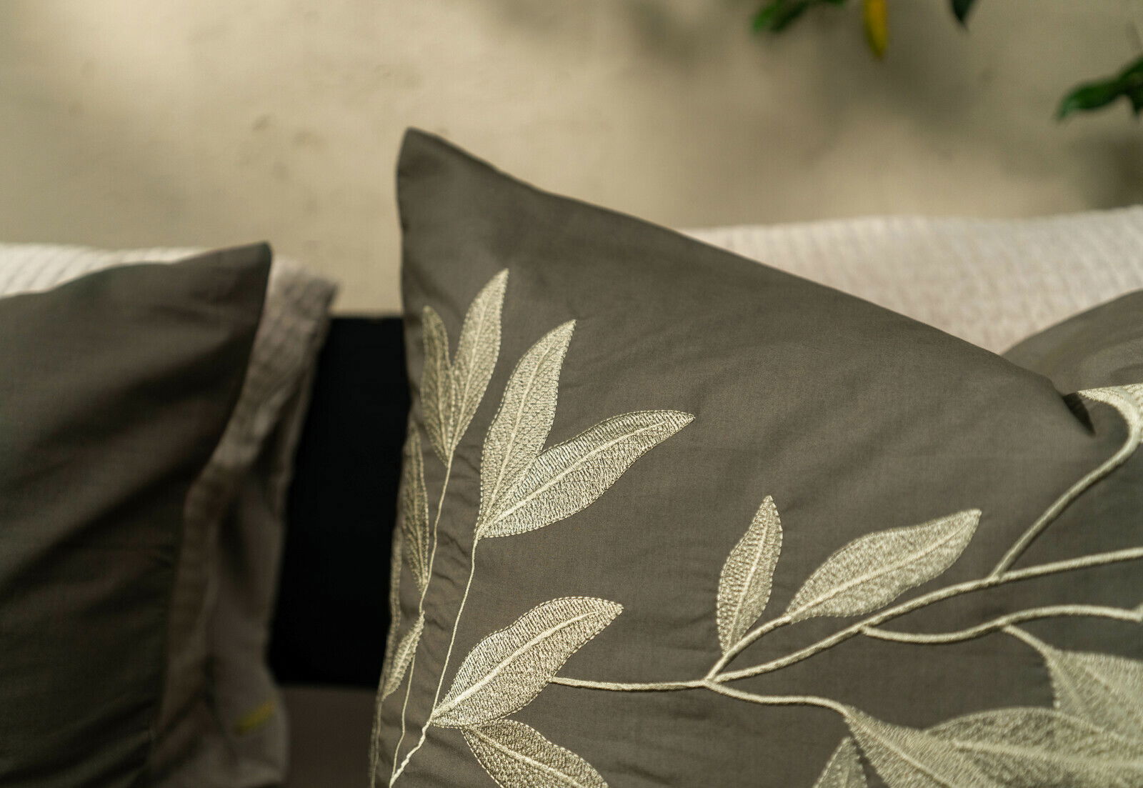Nahaufnahme von Bettwäsche mit gesticktem Blattmuster in Grau- und Beigetönen, seitliche Perspektive.
