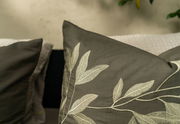 Nahaufnahme von Bettwäsche mit gesticktem Blattmuster in Grau- und Beigetönen, seitliche Perspektive.