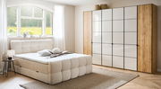 Modernes Boxbett in einem hellen Schlafzimmer mit großem Fenster, beige gepolstertem Kopfteil und passendem Teppich, seitliche Perspektive.