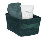 Dunkelgrüner Badkorb Anela mini, gefüllt mit einem Handtuch und einer Tube, aus schräger Perspektive fotografiert.