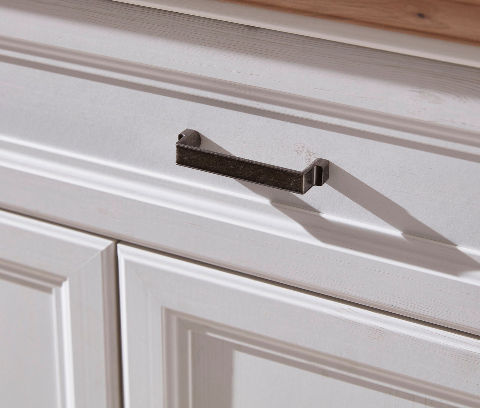Nahaufnahme eines weißen Schranks mit einer dunklen Metallgriffleiste, von schräg oben fotografiert.
