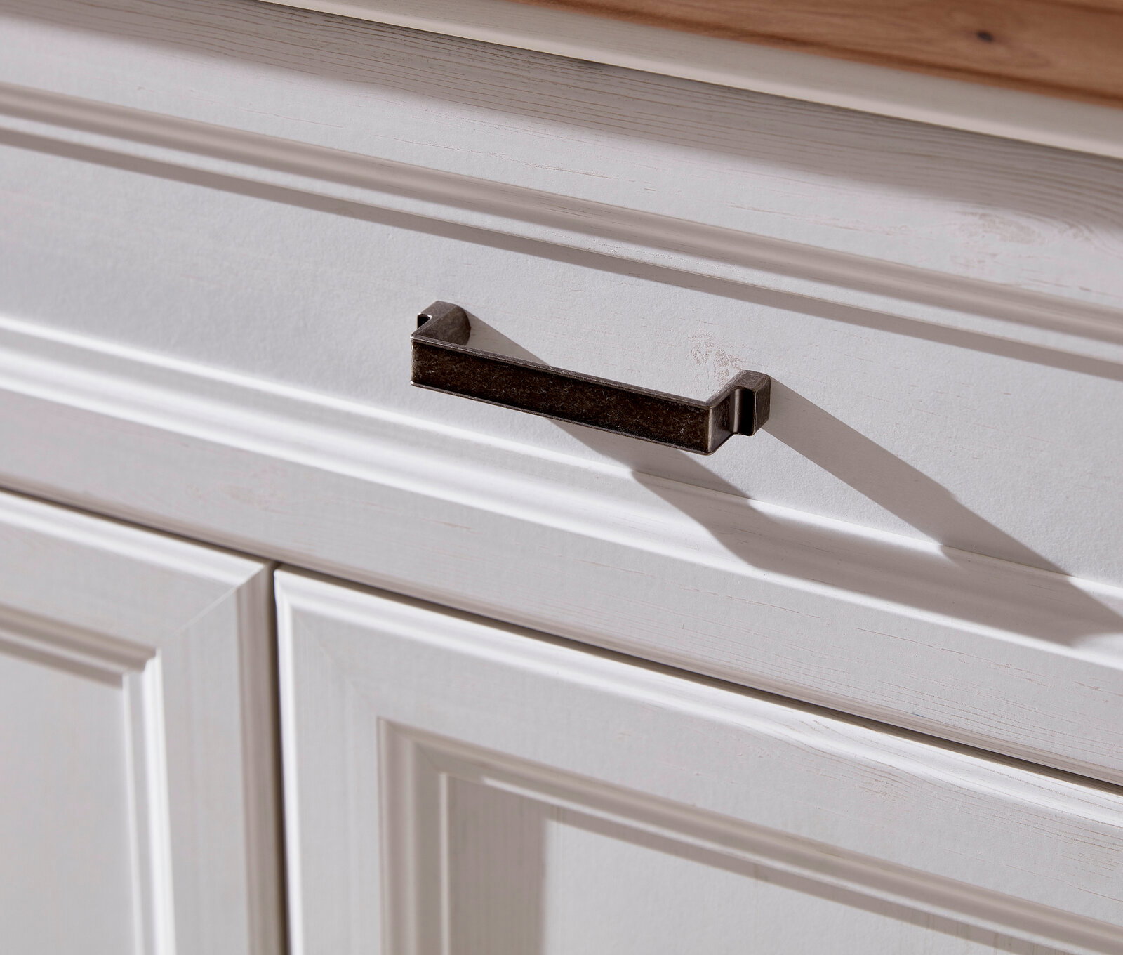 Nahaufnahme eines weißen Schranks mit einer dunklen Metallgriffleiste, von schräg oben fotografiert.