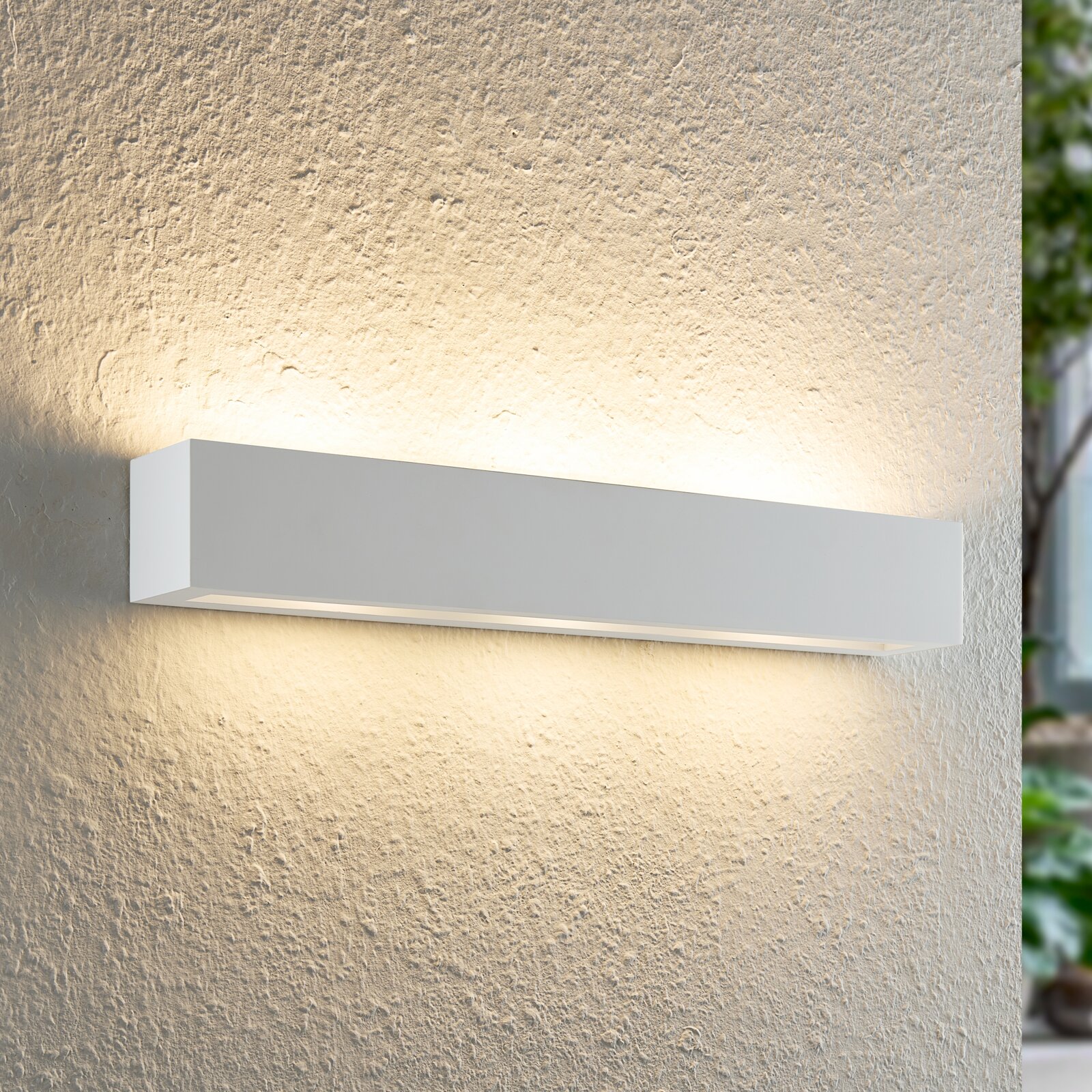 Moderne weiße Wandleuchte mit rechteckigem Design, die warmes Licht nach oben und unten auf eine strukturierte Wand abstrahlt. Seitliche Perspektive.