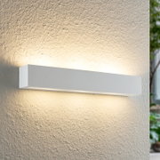 Moderne weiße Wandleuchte mit rechteckigem Design, die warmes Licht nach oben und unten auf eine strukturierte Wand abstrahlt. Seitliche Perspektive.