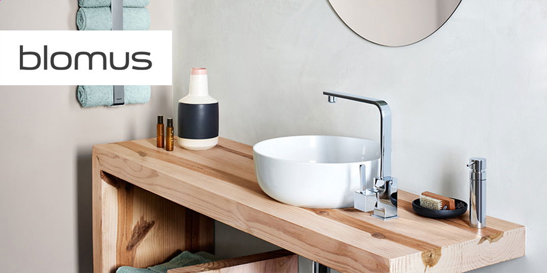 Ein Außenbereich mit einer Holzterrasse, Sitzgelegenheiten mit dekorativen Kissen und dem  blomus Logo.