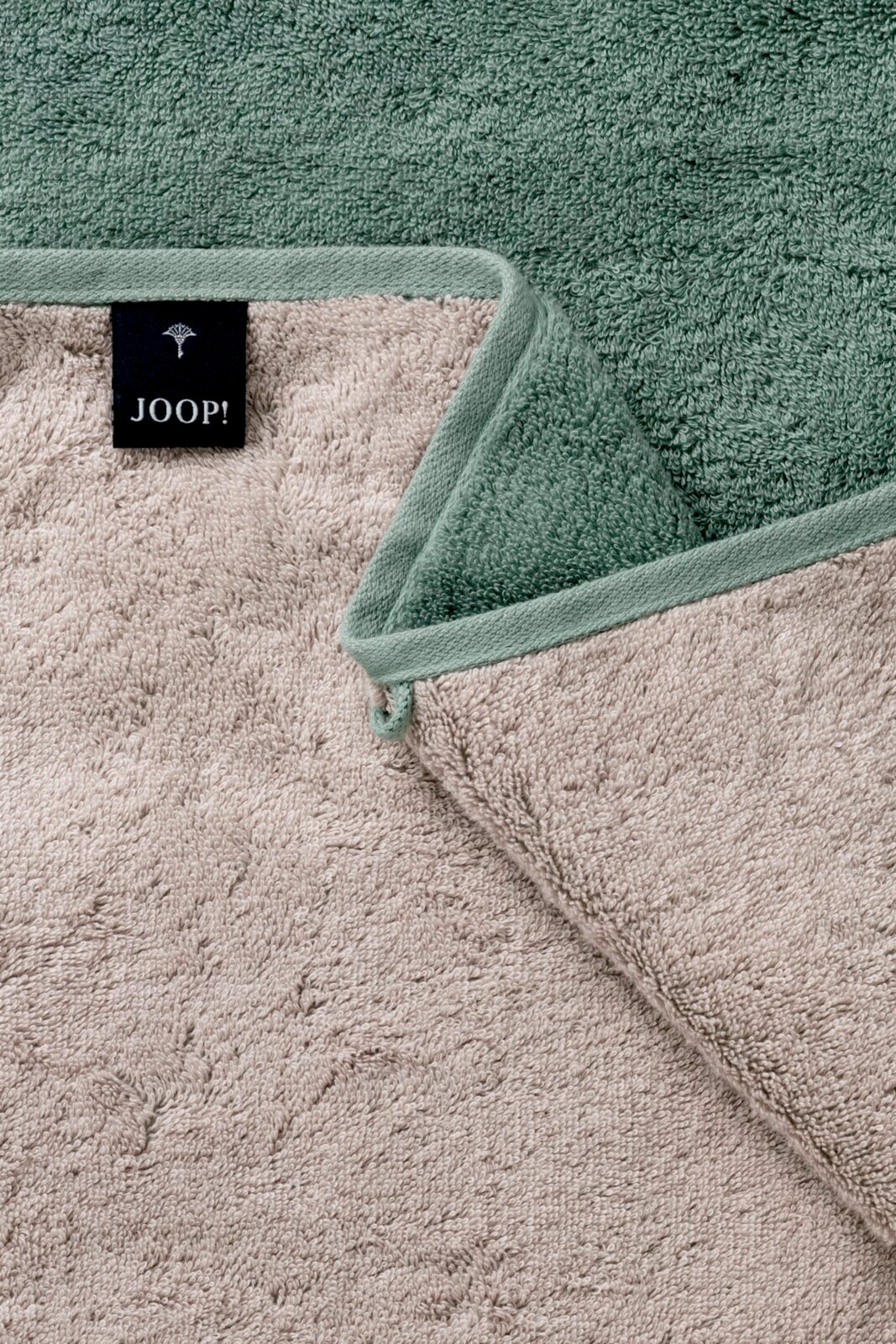 Close-up van een tweekleurige douchehanddoek met een label van het merk JOOP! in groen en beige.