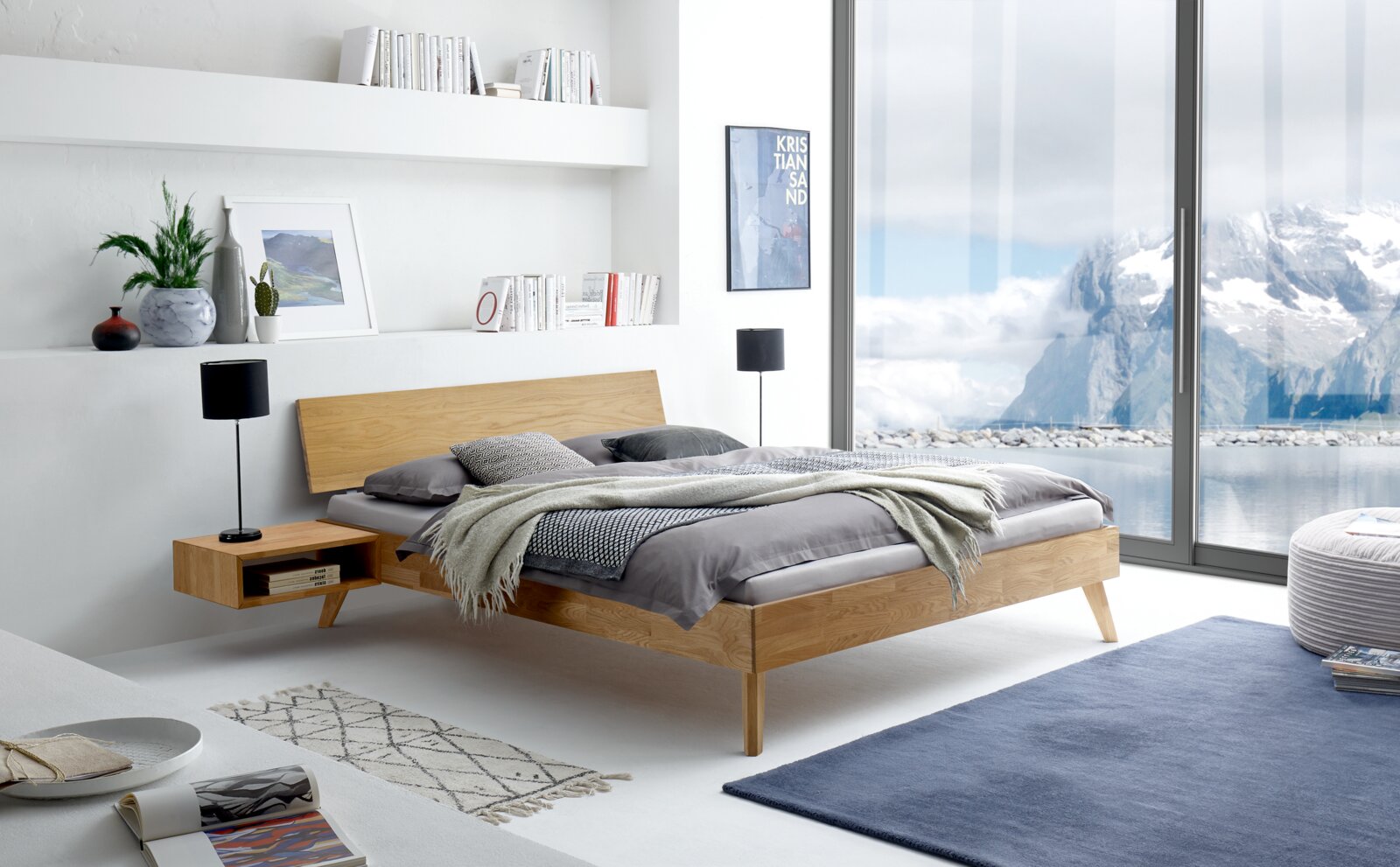 Modern houten bedframe in een lichte, minimalistische slaapkamer met uitzicht op een besneeuwd berglandschap door grote ramen. Zijaanzicht.