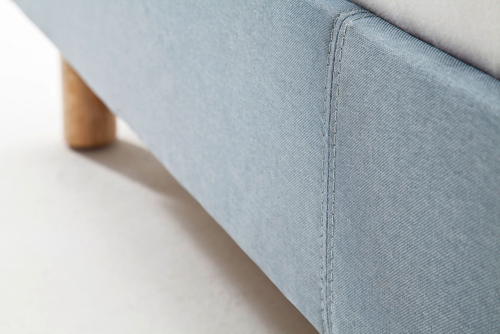 Nahaufnahme eines blauen Polsterbetts mit Holzfuß, seitliche Perspektive