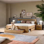 Modernes Holzbett in Eiche-Optik mit hohem Kopfteil, integrierten Schubladen und Nachttisch im Schlafzimmer, frontale Perspektive auf das Bett