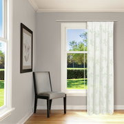 Heller Raum mit einem großen Fenster, durch das ein Vorhang mit grünem Blattmuster hängt. Ein grauer Stuhl steht in der Ecke. Perspektive von innen nach außen.